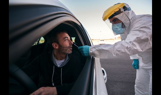 Lab tech in protective gear checks patient in car