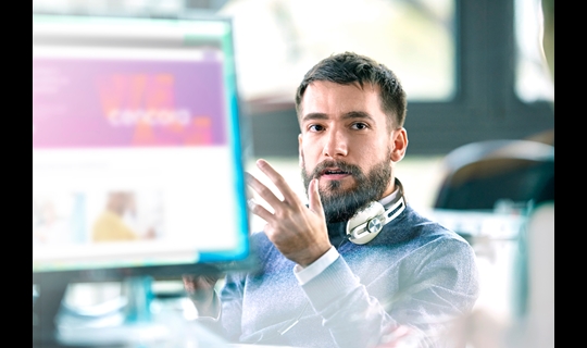 Man with beard and headphones sitting in front of computer in office