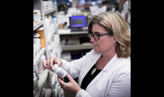 Pharmacist examining a pill bottle behind the pharmacy counter