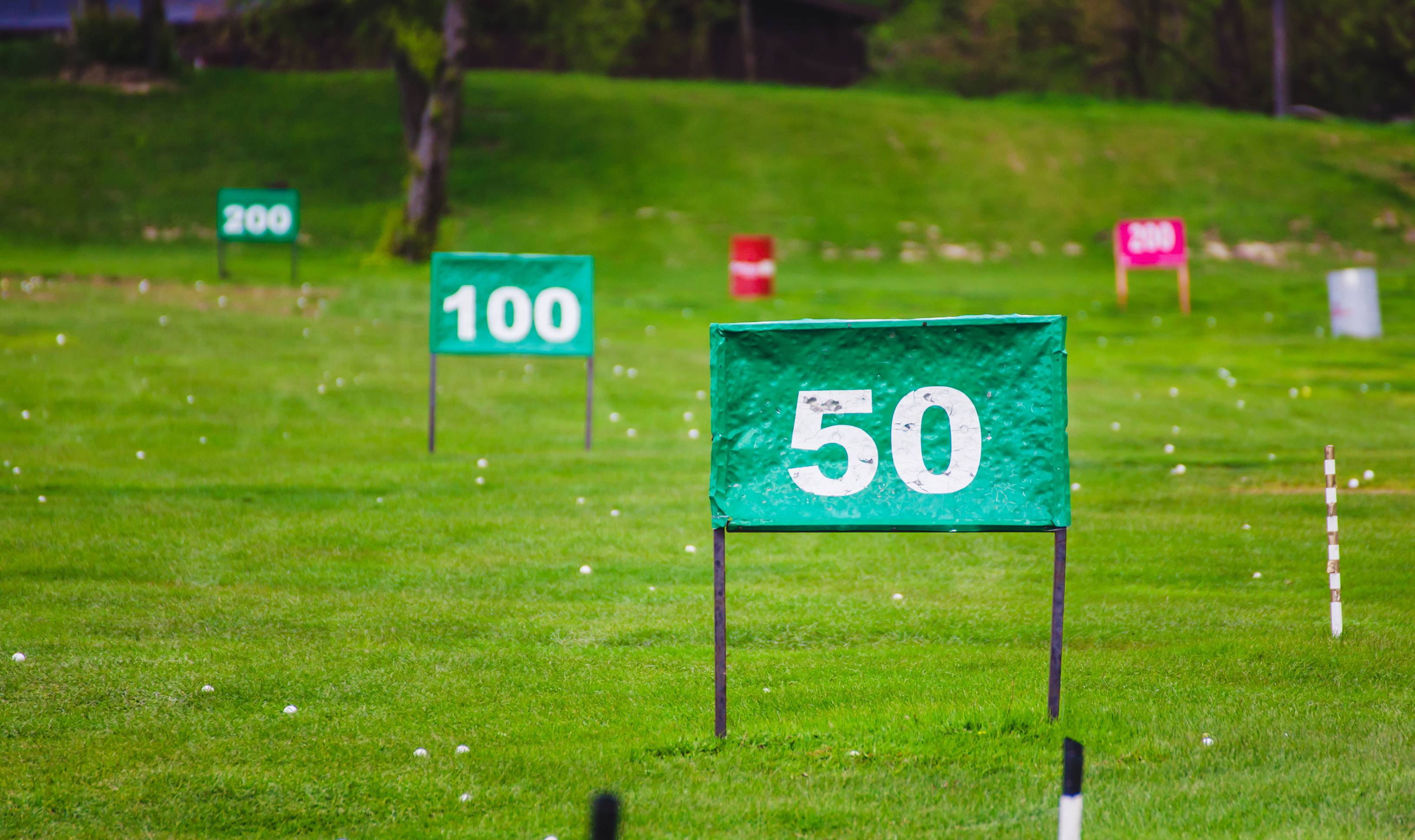 Distance markers laid out on a driving range with golf balls strewn across the grass