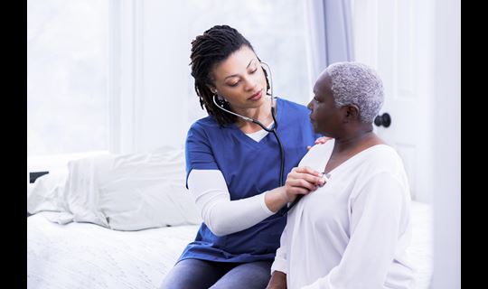 Black female nurse uses stethoscope on older Black female patient